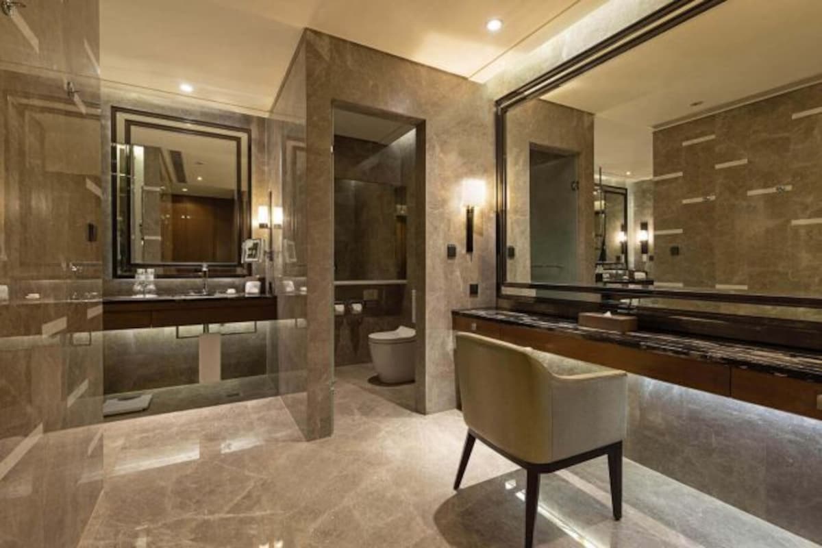 Une salle de bain moderne avec un grand miroir, un sol en marbre et une coiffeuse avec un fauteuil.