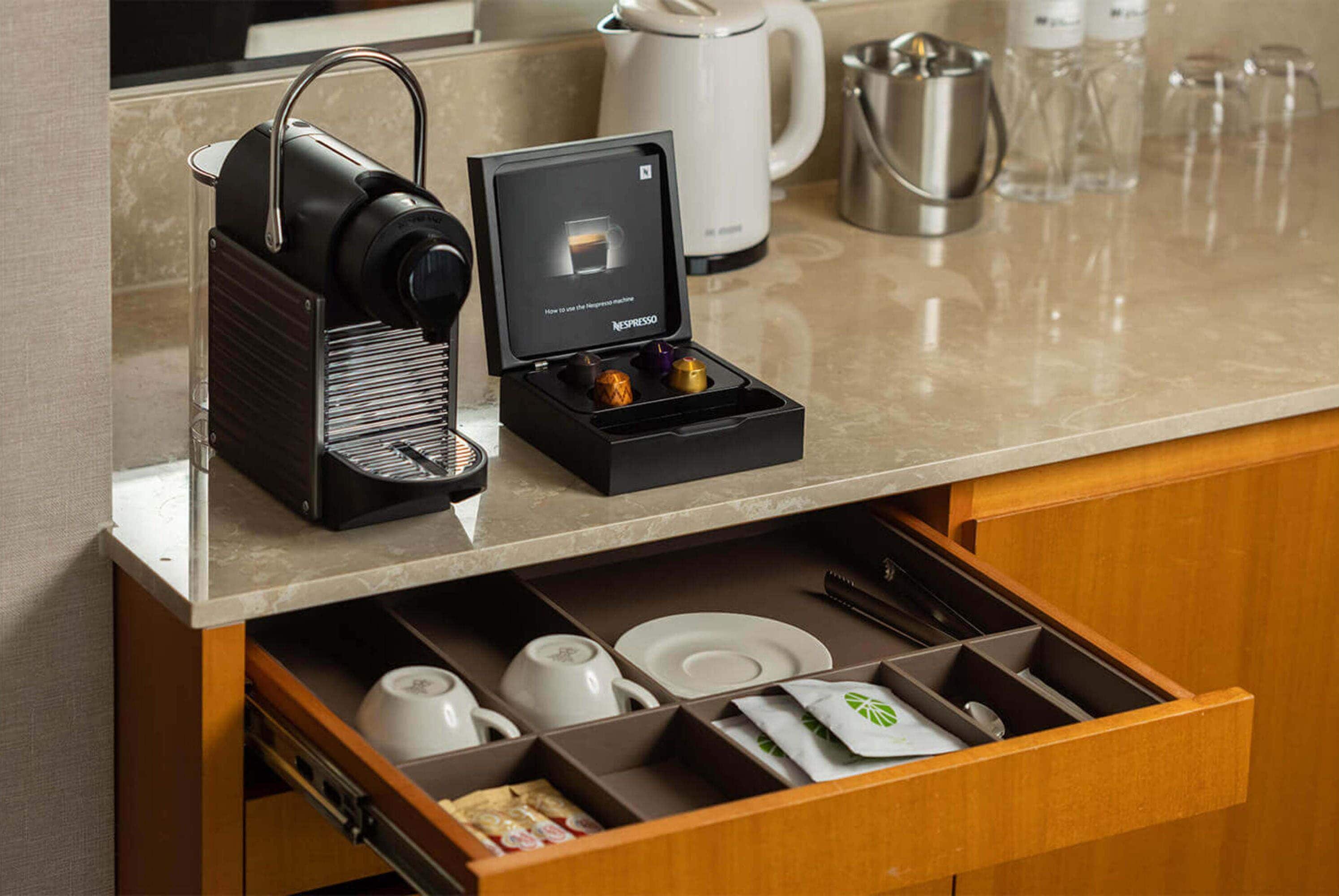 A kitchen with a coffee machine, a kettle, and a drawer containing various kitchen items.