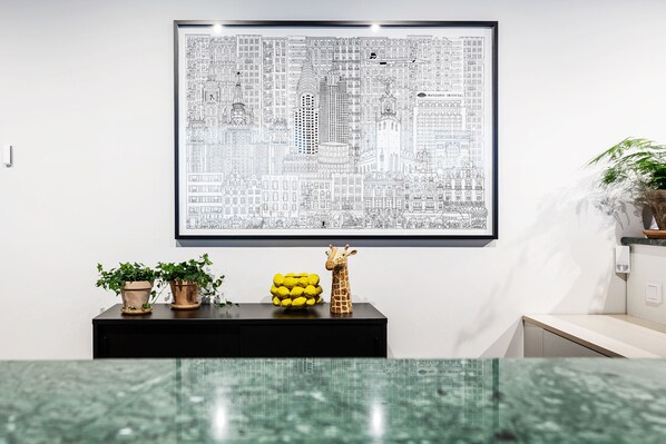 A framed cityscape artwork on a wall, a black console table with potted plants and a yellow fruit bowl, and a green patterned floor. - Biz Apartment Bromma (Bromma)