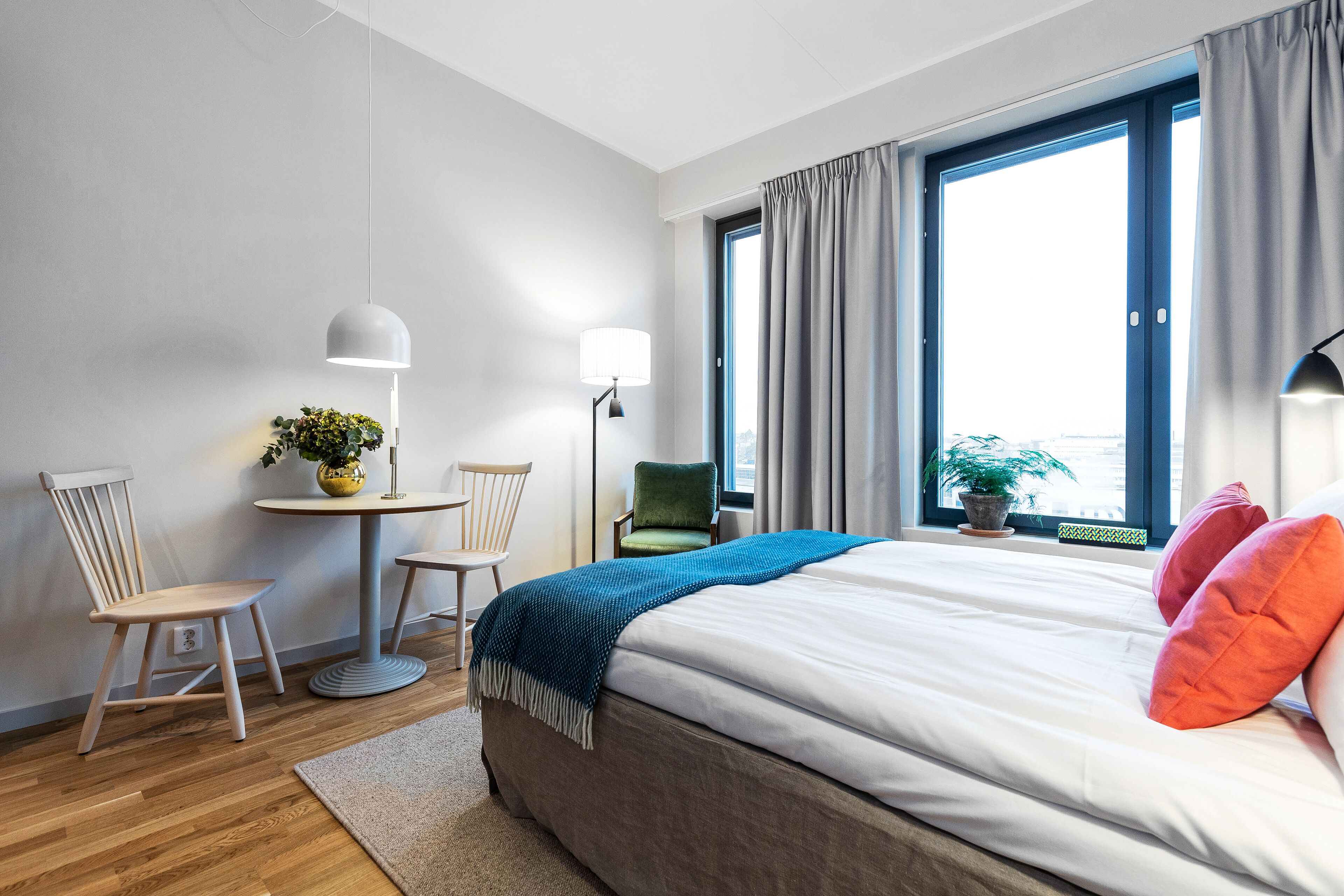 Ein modernes Hotelzimmer mit einem großen Bett, zwei Sesseln, einem kleinen Tisch und einer Zimmerpflanze.