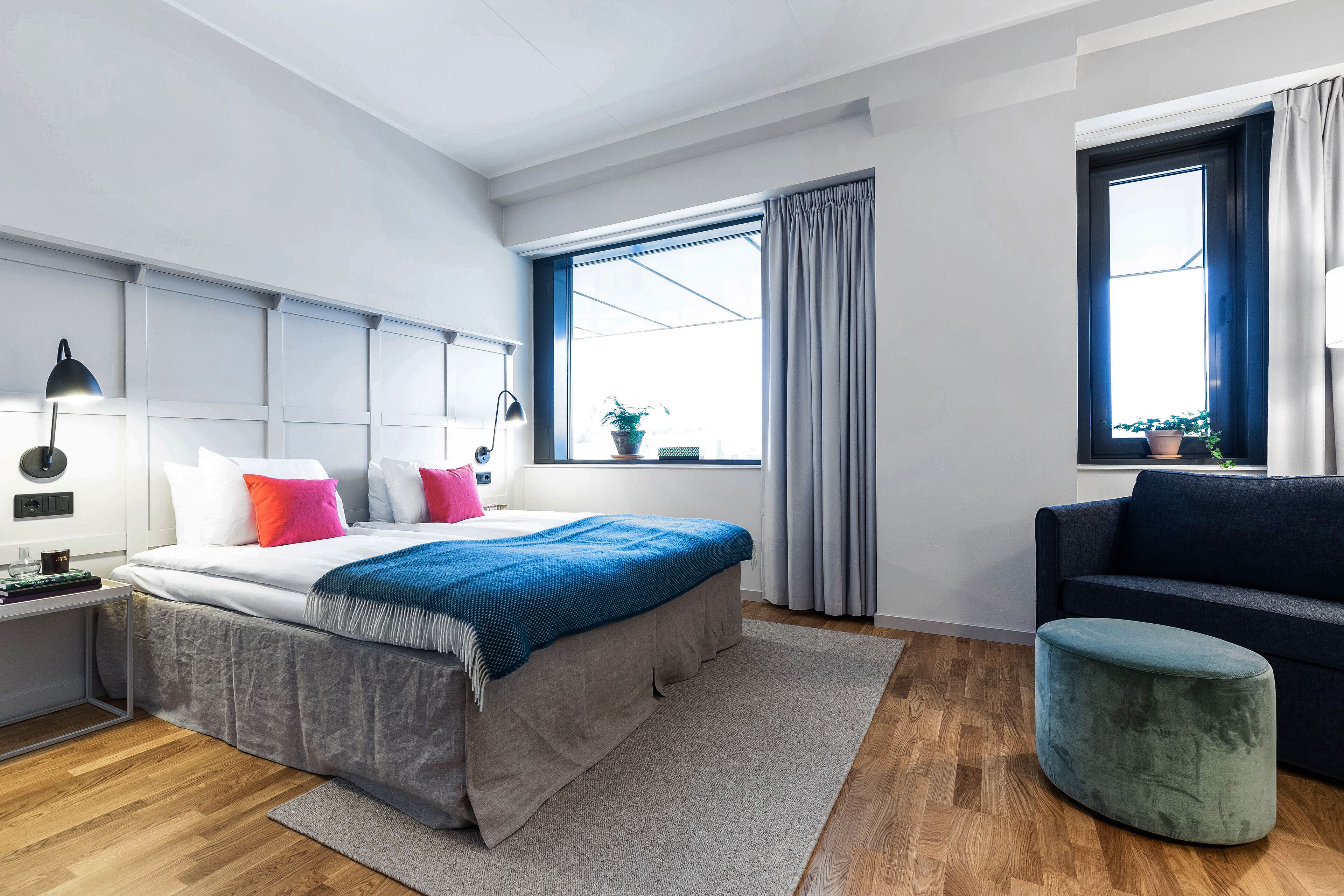 A modern bedroom with a bed, bedside table, lamp, and a view of the outdoors through a window.