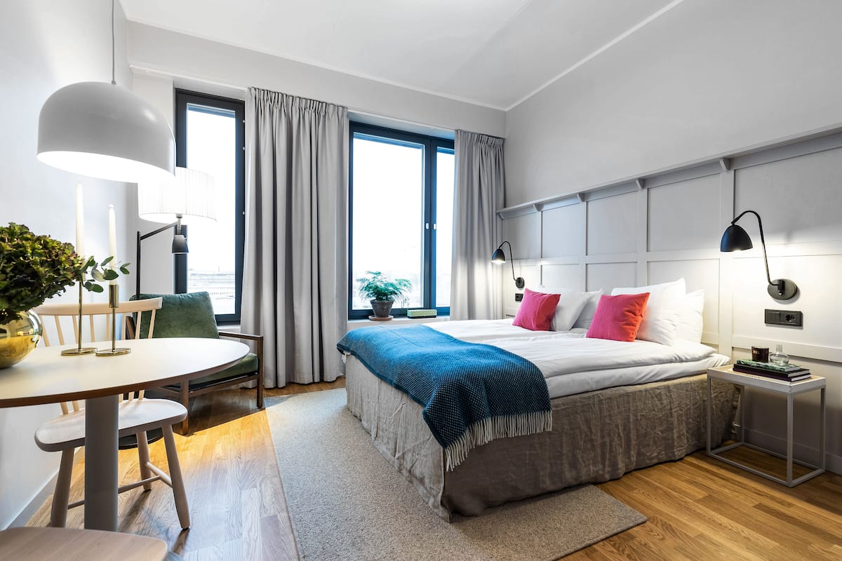 Un dormitorio moderno con cama, mesitas de noche, un escritorio y una ventana con cortinas.