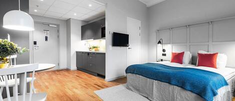 A modern hotel room with a large bed, a desk, and a kitchenette.