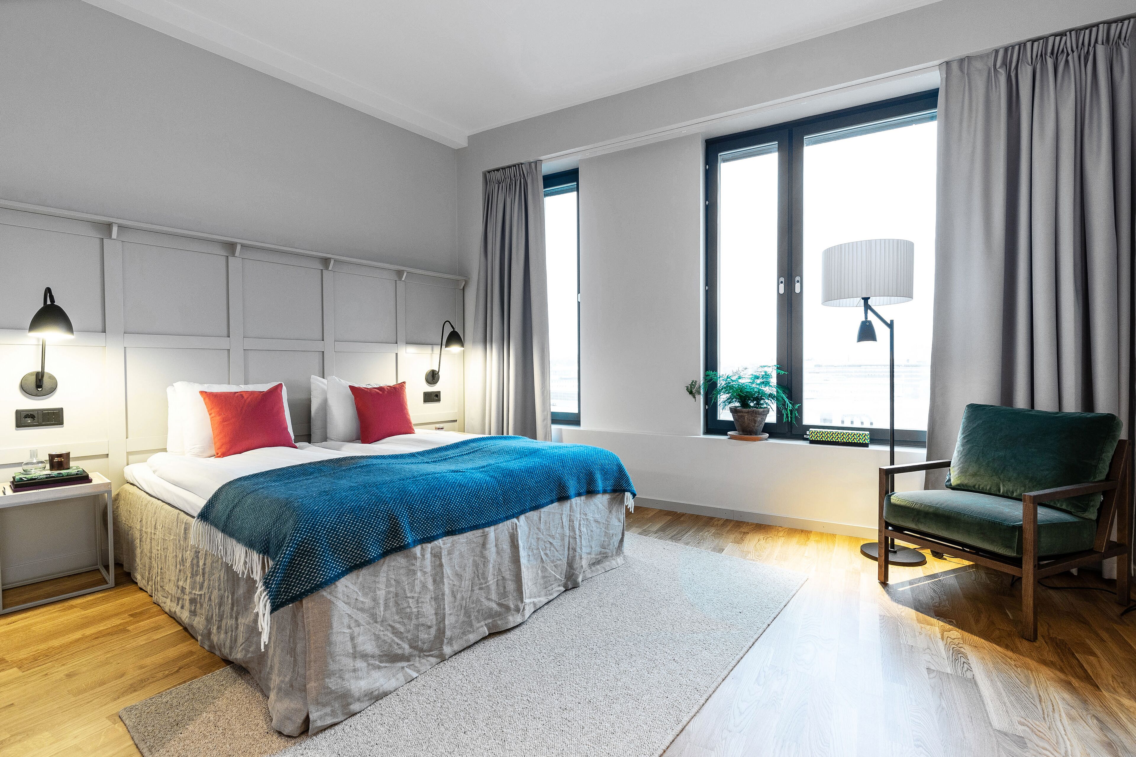 A modern bedroom with a large bed, bedside lamps, a green chair, and a window with curtains.