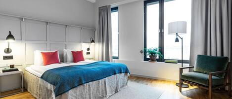 A modern bedroom with a large bed, bedside lamps, a green chair, and a window with curtains.