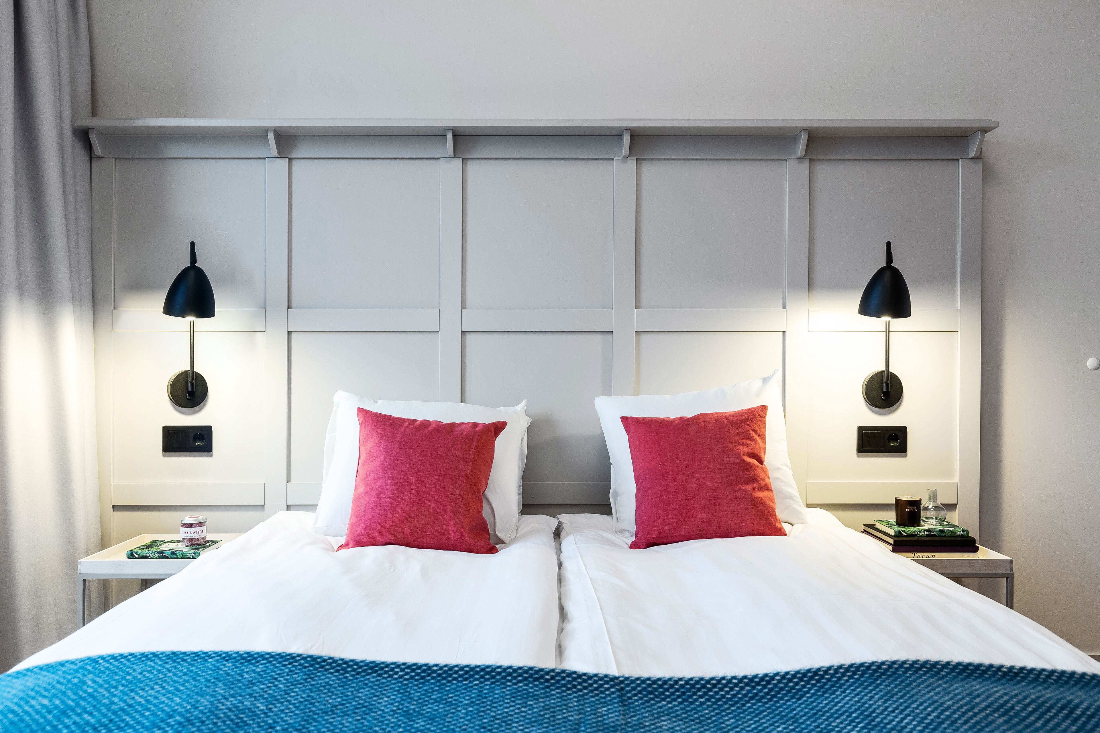 A double bed with white and red pillows, two bedside tables with lamps, and a blue and white bedspread.