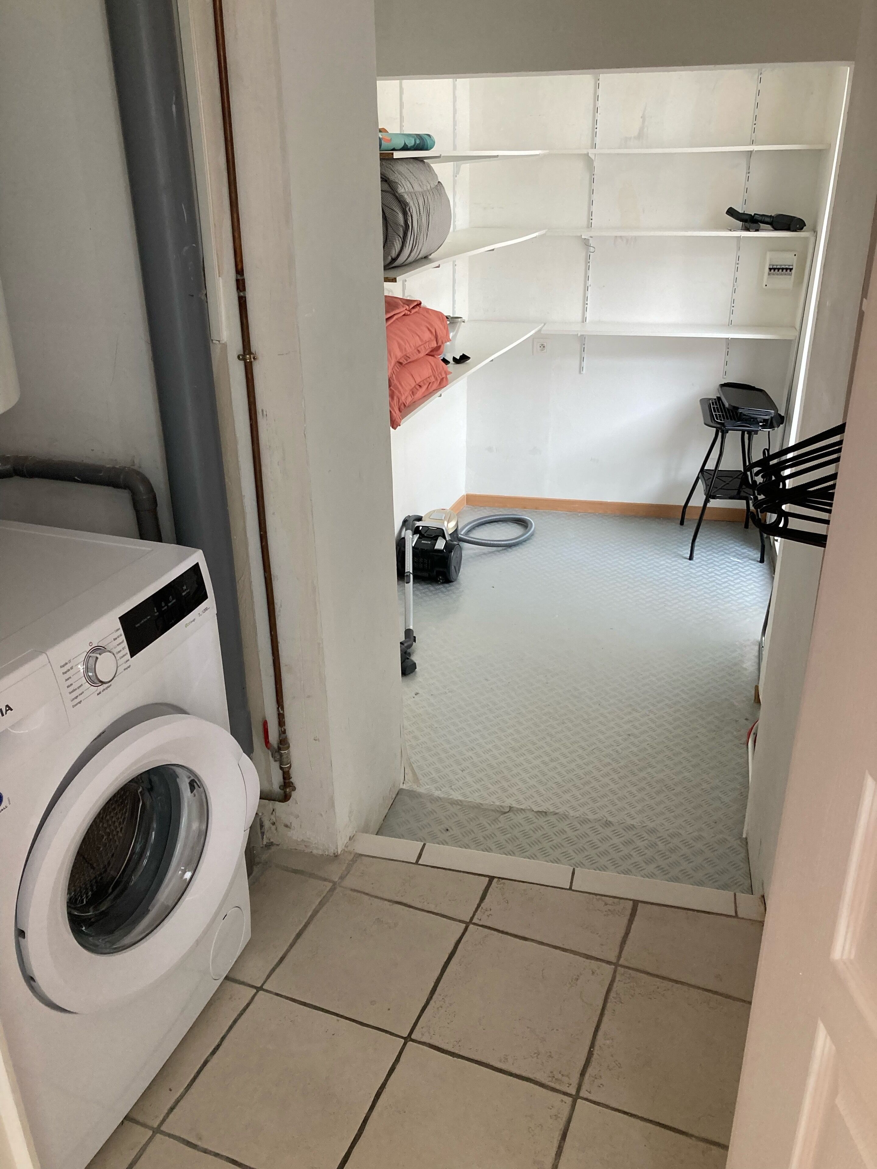 Un espace buanderie comprenant un lave-linge, un aspirateur et une petite table avec une chaise.