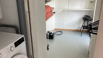 Un espace buanderie comprenant un lave-linge, un aspirateur et une petite table avec une chaise.