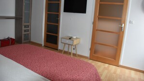 Ett sovrum med en säng, ett skrivbord, en garderob och en tv på väggen.