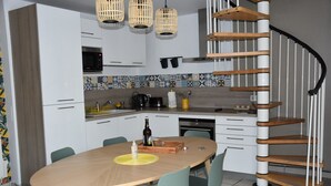 Ett kompakt kök med mikrovågsugn, spis och diskho. Här finns ett matbord med stolar, en spiraltrappa och en kakelbeklädd vägg bakom arbetsbänken.