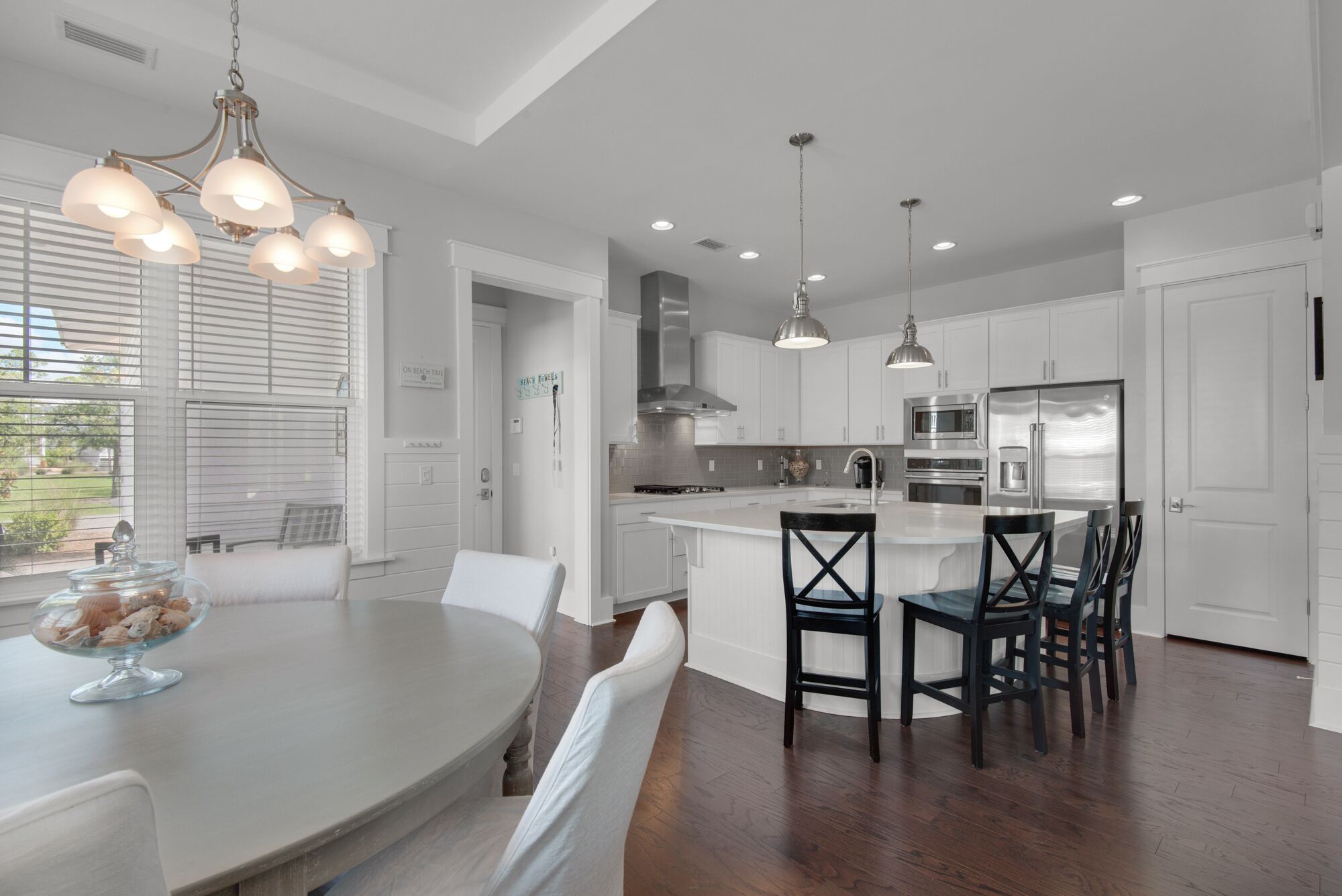 Une cuisine moderne avec des meubles blancs, un îlot central doté de tabourets et des luminaires suspendus.