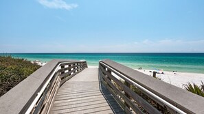 A wooden boardwalk leading to a beach with clear turquoise water and a sandy shore.