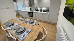Una cocina moderna con armarios blancos, una mesa de comedor de madera preparada para cuatro personas y un horno empotrado.