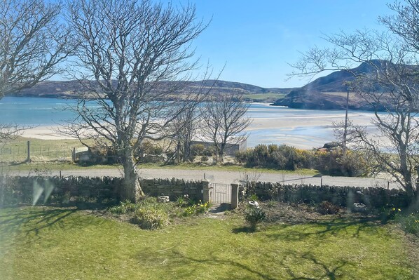 A coastal landscape with a stone wall, a grassy area, and a clear view of the sea and distant hills.