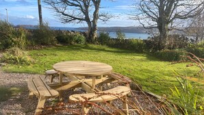 Una mesa de picnic de madera con bancos en un área verde con vista a un lago y colinas.