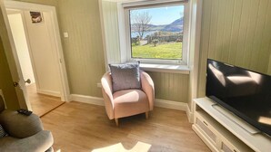 Una habitación con ventana, televisor, silla y puerta.