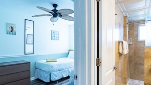 A bedroom with a bed, a ceiling fan, a dresser, and a bathroom with a shower and towel rack. - Lazy Livin 6 · Pool 50 Ft Away · 2-Min Beach (Bradenton Beach)