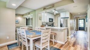 Een moderne keuken met witte kasten, een centraal eiland en een eetgedeelte met een houten tafel en stoelen.