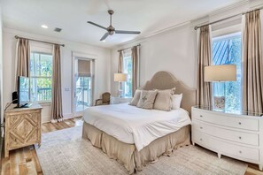 Ein geräumiges Schlafzimmer mit einem großen Bett, einem Deckenventilator und Blick ins Freie durch die Fenster.
