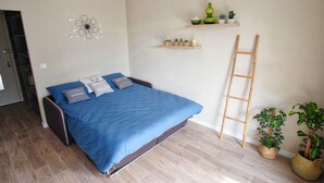 Un dormitorio con cama, almohadas, estante en la pared con plantas, una escalera y una puerta a otra habitación.