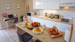 Una cocina moderna con armarios blancos, una mesa de comedor con cruasanes, fruta y una computadora portátil.