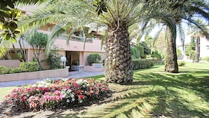 A well-maintained garden with palm trees, a pathway, and a building with a balcony. - (029) L'entre deux à 4 (Antibes)