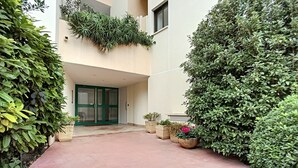 A building entrance with a glass door, surrounded by lush greenery and potted plants.