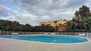 A swimming pool with a paved deck, surrounded by a white fence and benches.