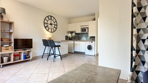 A compact living space with a kitchen, a dining area with a TV and bar stools, and a laundry machine.