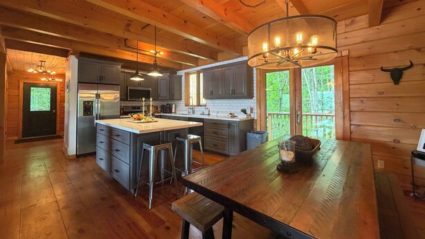 Une cuisine spacieuse avec des poutres en bois, un grand îlot central, des tabourets de bar et un lustre.