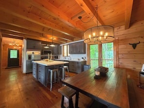 A spacious kitchen with wooden beams, a large island, bar stools, and a chandelier.