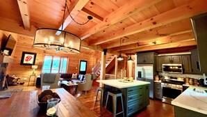 Un intérieur spacieux de chalet en bois, comprenant une cuisine, un coin repas et un escalier menant à une mezzanine.