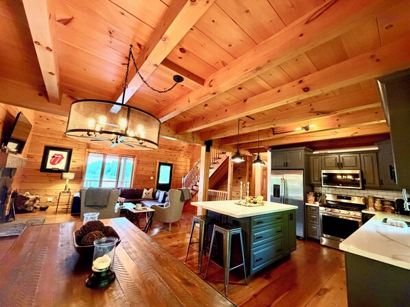 A spacious log cabin interior with a kitchen, dining area, and a staircase leading to a loft.