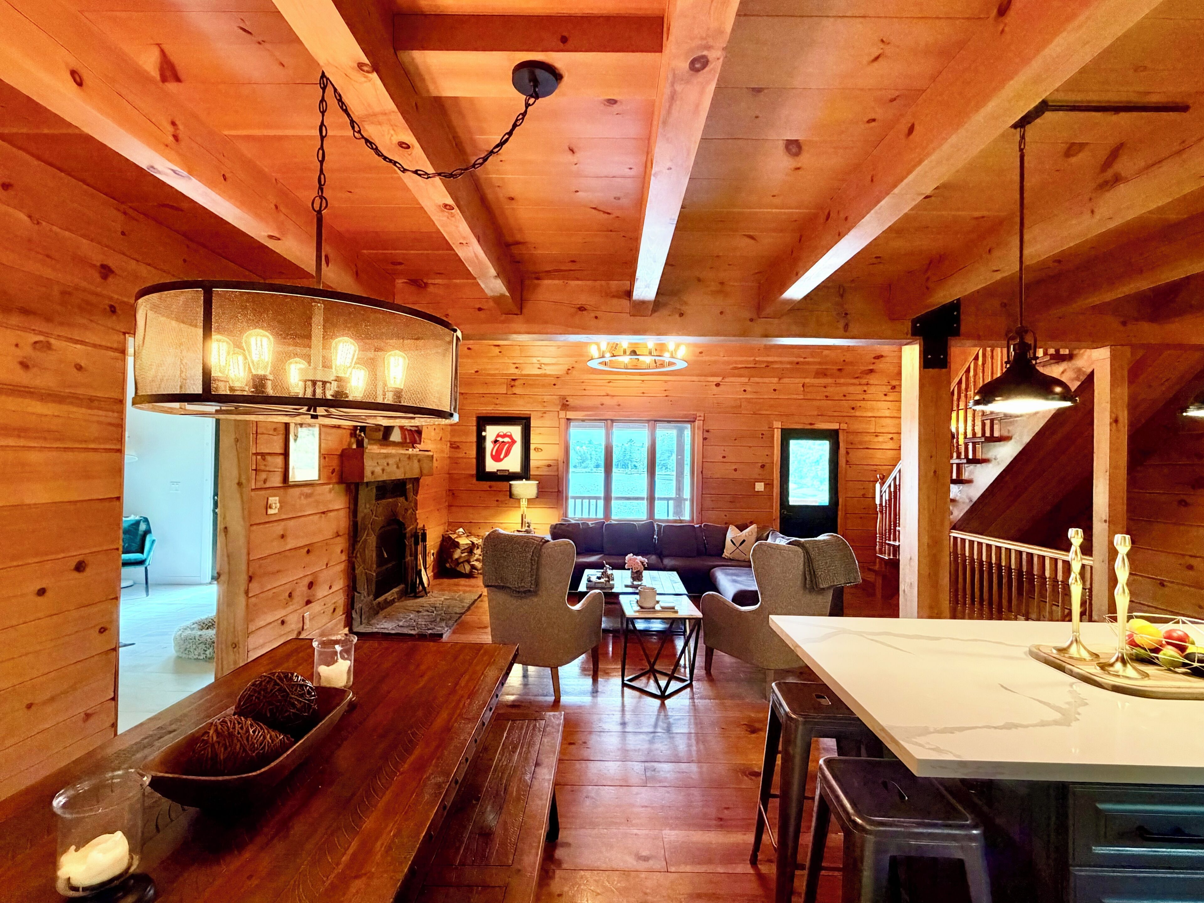 Un intérieur de chalet chaleureux, avec un revêtement en bois, une cheminée, un coin repas et une cuisine dotée d’un bar.