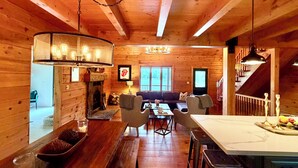 Un intérieur de chalet chaleureux, avec un revêtement en bois, une cheminée, un coin repas et une cuisine dotée d’un bar.