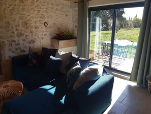 Ein gemütliches Wohnzimmer mit einer Steinwand, einem blauen Sofa und Blick auf einen Garten durch eine Glastür.