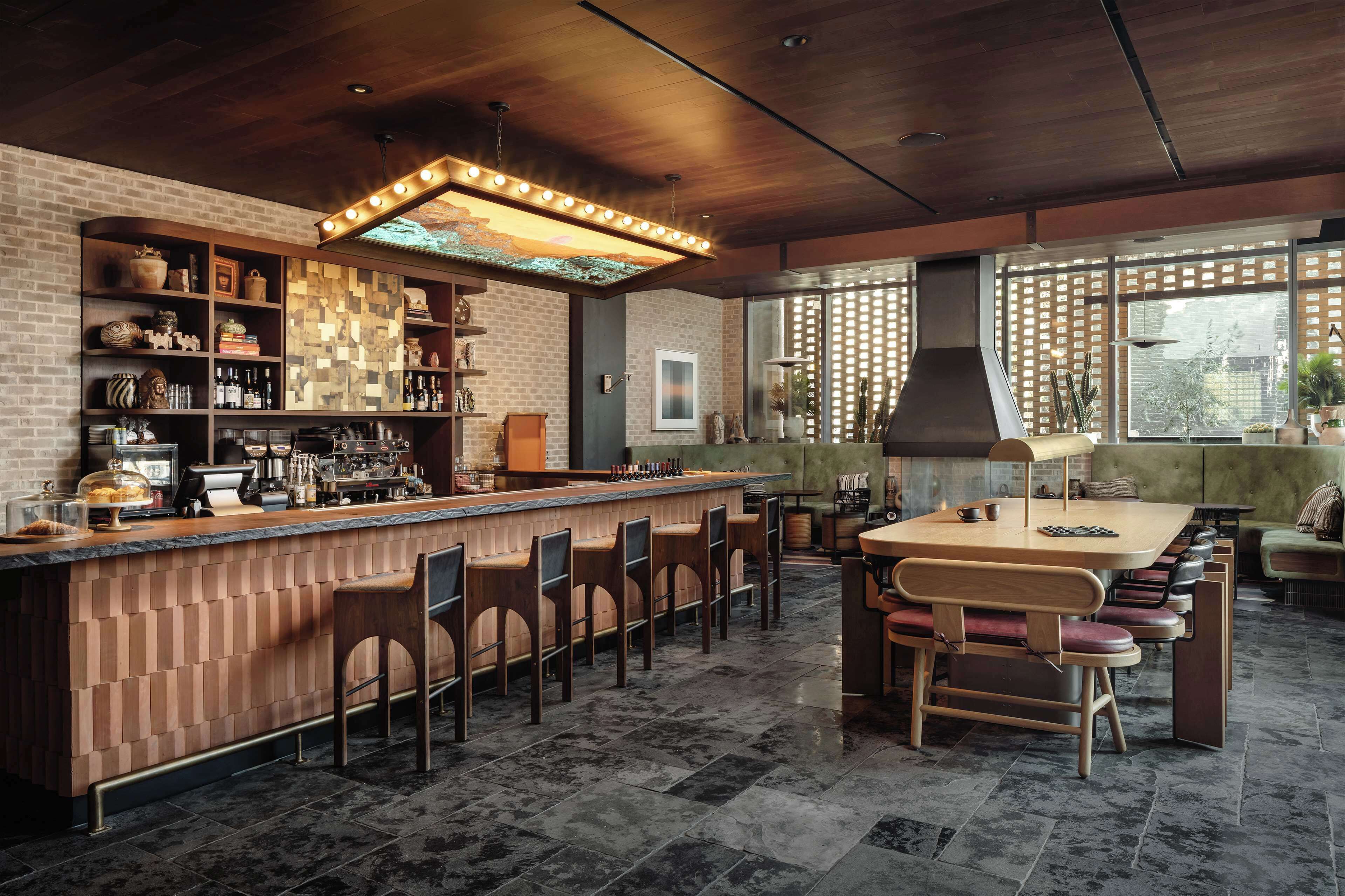A bar area with a wooden counter, bar stools, and a large window with a view of the outside.