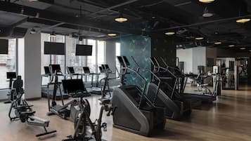 A modern gym with various cardio machines, large windows, and a clean, industrial design.