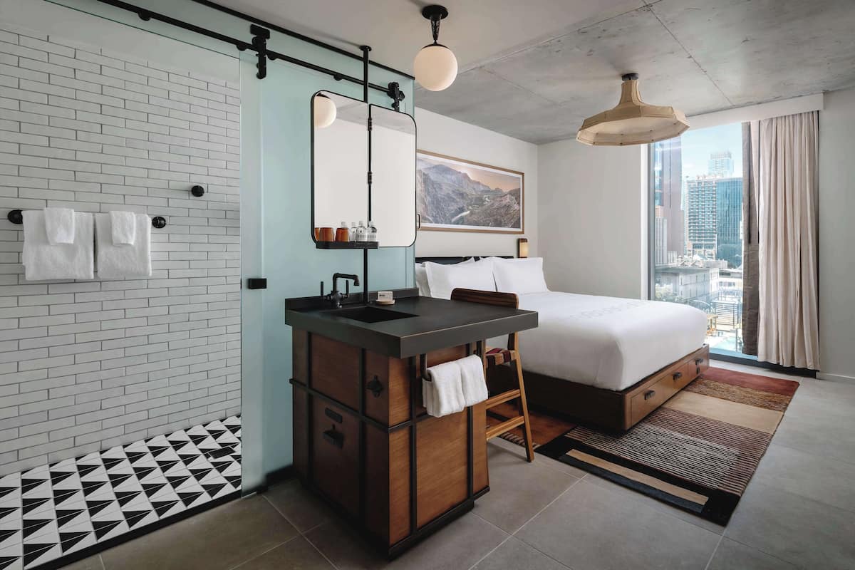 Une chambre d’hôtel moderne, équipée d’un lit, d’une coiffeuse avec un miroir, d’un lavabo et offrant une vue sur la ville.