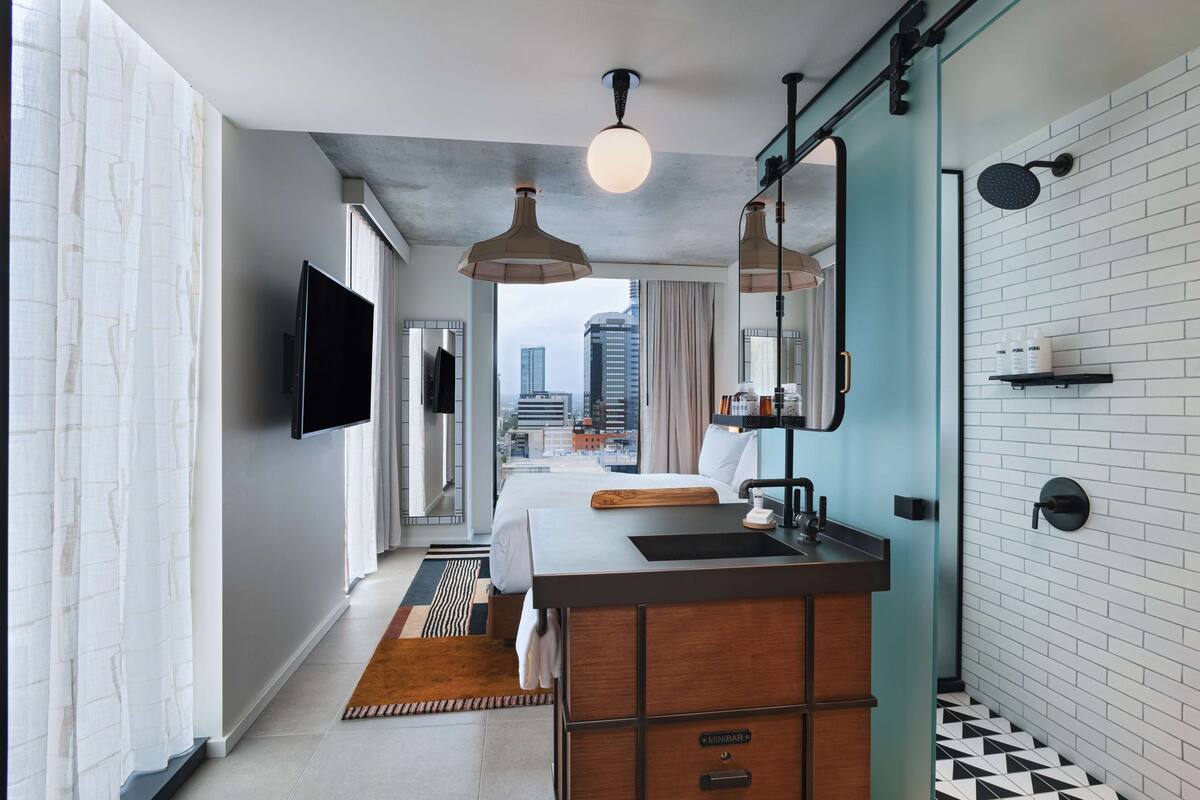 Une chambre d’hôtel moderne dotée d’un grand lit, d’une coiffeuse en bois, d’un téléviseur à écran plat et offrant une vue sur la ville.