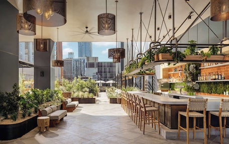 A modern bar area with seating, plants, and a city view.