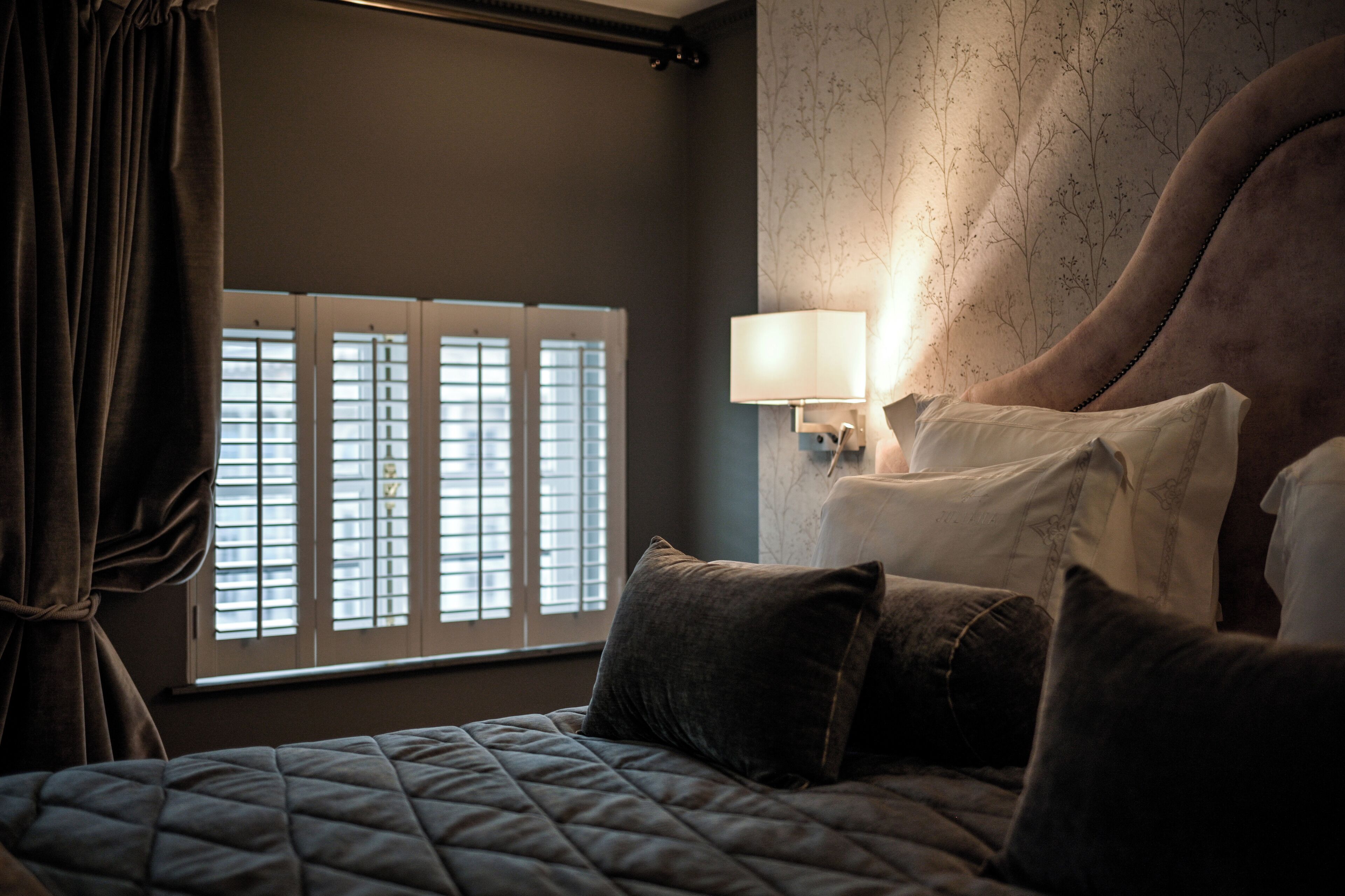 Un dormitorio con una cama grande, una mesita de noche con lámpara y una ventana con persianas.