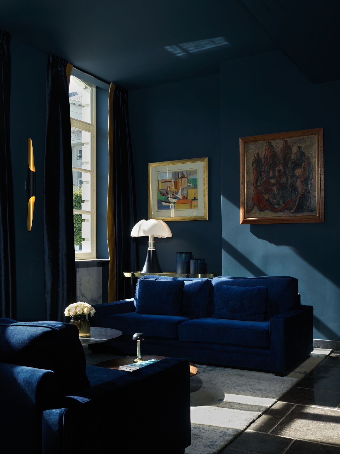 A modern living room with a blue sofa, a lamp, and artwork on the walls.