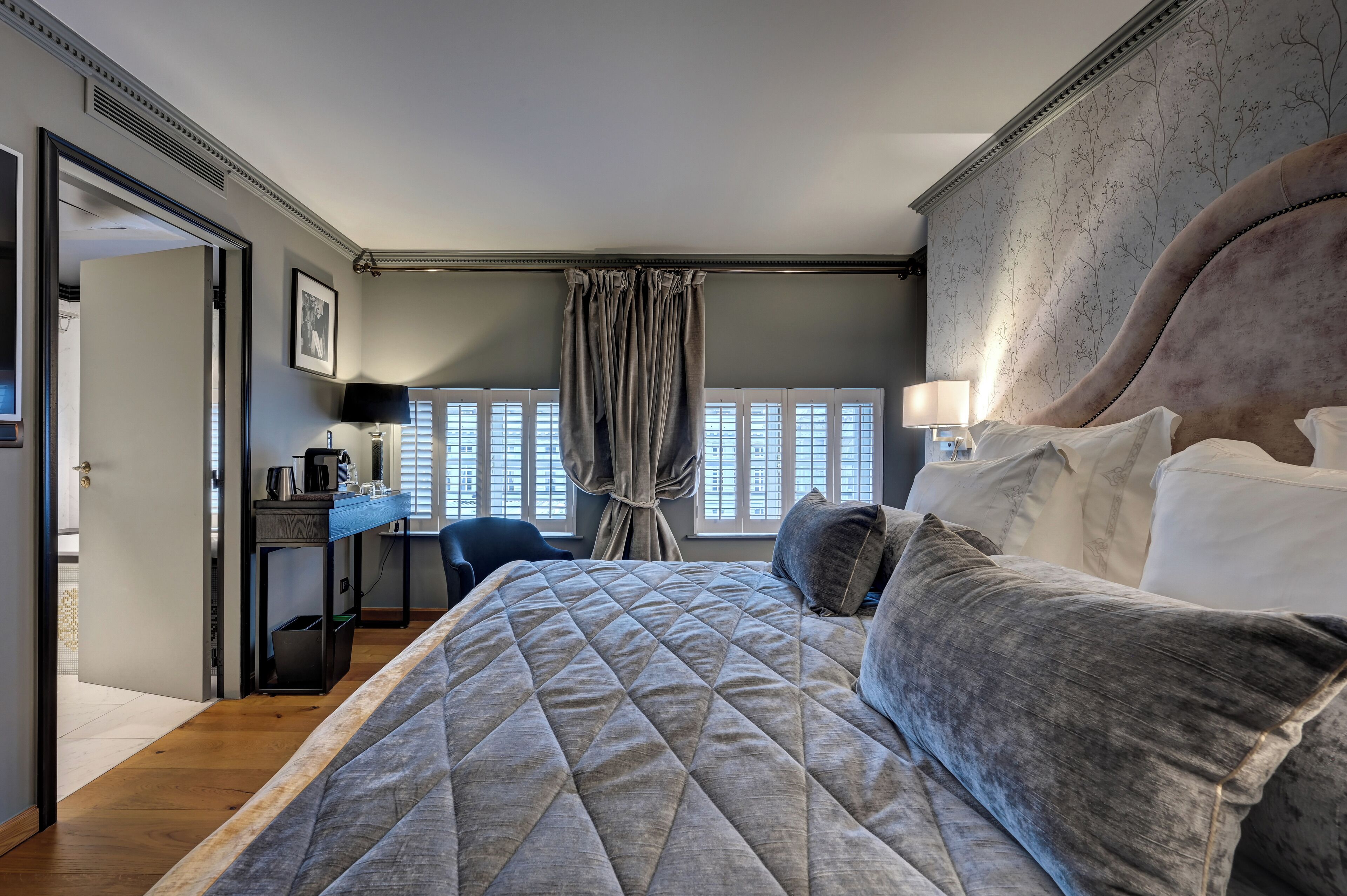 Quarto com cama grande, escrivaninha, cadeira e janela com cortinas.