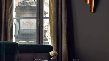 A dining area with a view of a statue through a window, a vase with a single flower, and a table set for two.
