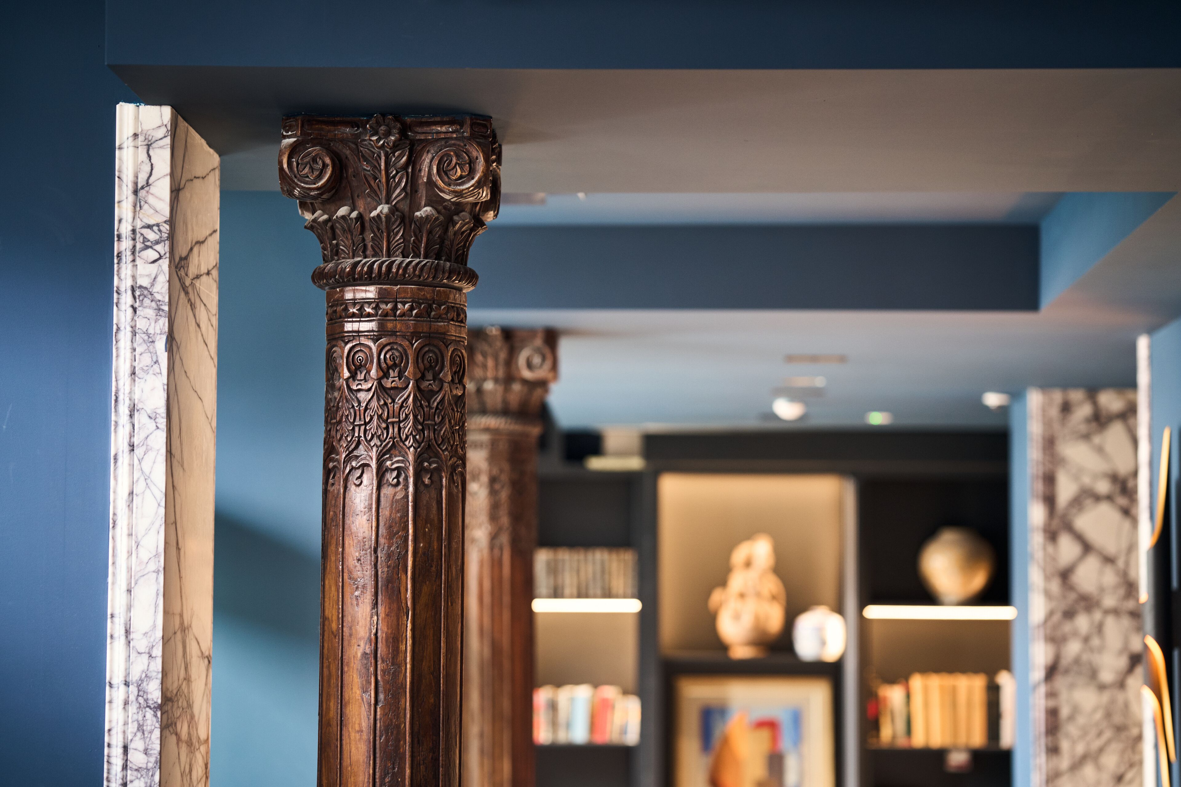 A marble column with intricate carvings, a bookshelf with books, and a decorative globe in a room with blue walls.