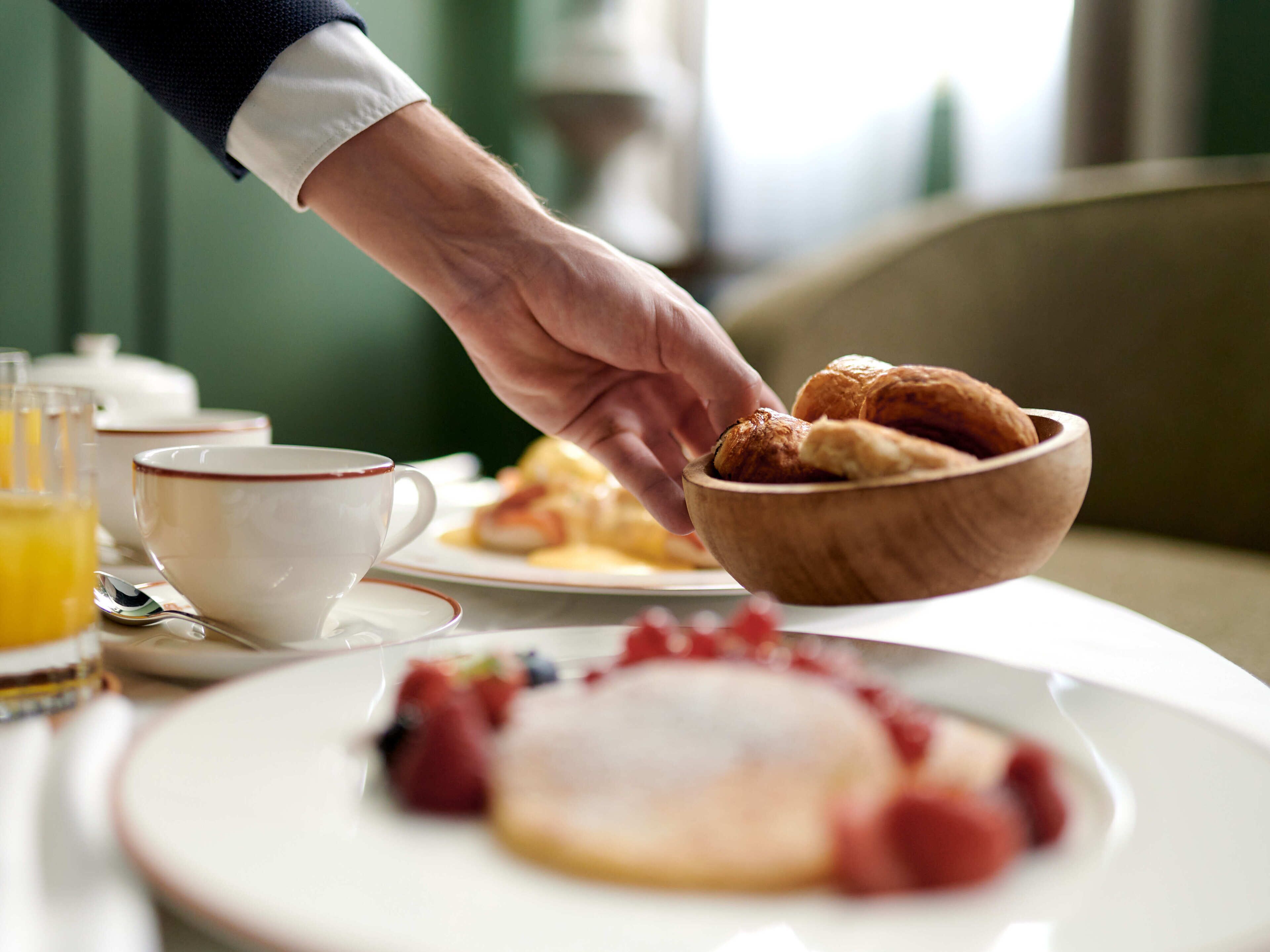 A breakfast setting with a wooden bowl of pastries, a plate with berries, and a cup of coffee.