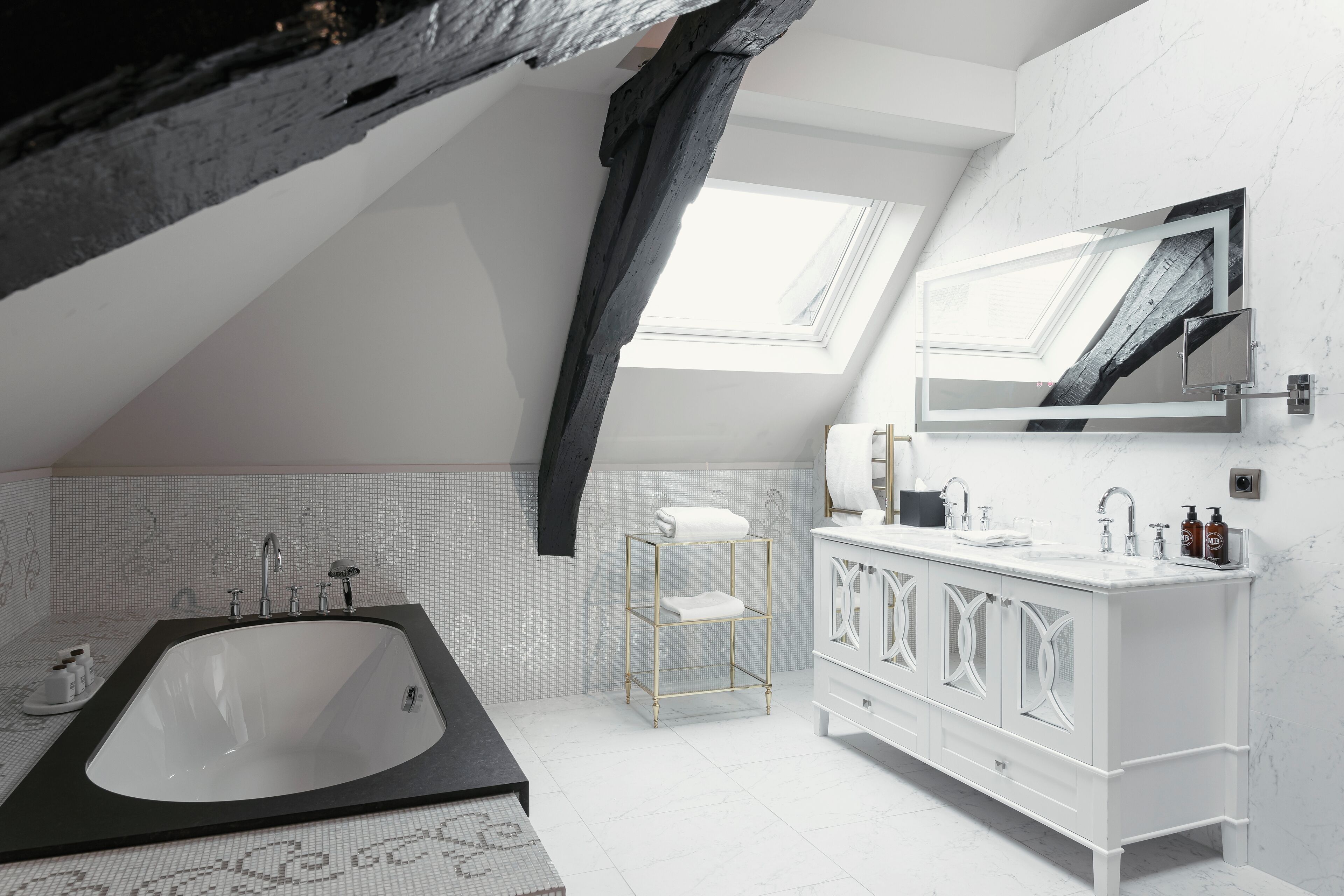 Een moderne badkamer met een vrijstaand bad, een wastafel met een grote spiegel en een dakraam.