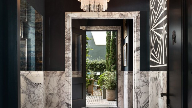 A hallway with a marble floor, a chandelier, and a view of an outdoor garden.