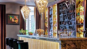 A bar area with a marble countertop, bar stools, decorative lighting, and a variety of bottles and glassware.